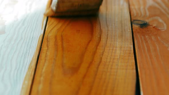 The painter technically applies wood stain on the freshly planed textured wooden board