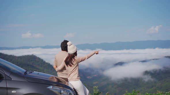 Young couple travelers with car watching a beautiful sea of fog over the mountain while traveling
