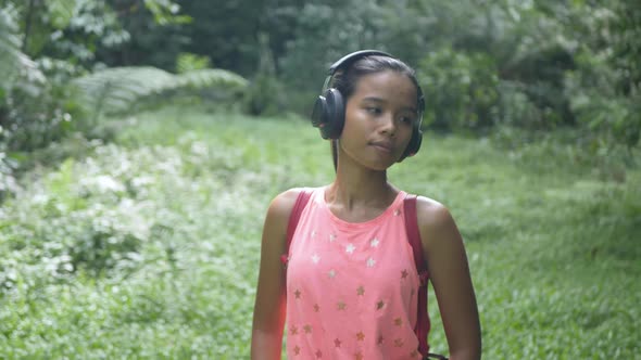 A Young Asian Girl Walks Through the Forest Listens to Music with Headphones Smiles and Goes Forward alt
