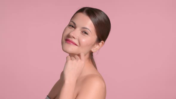 30s Brunette Woman Wears a Decollete Top with Ideal Skin in Studio on Pink Background