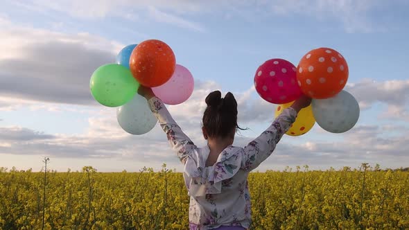 Girl in a Yellow Field Waving Her Hands with Balloons alt