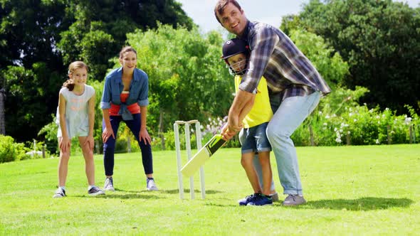 Family playing cricket in park alt
