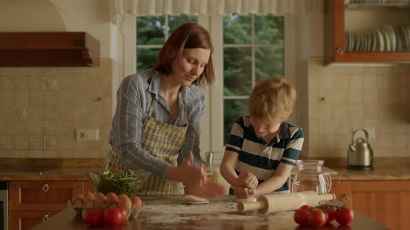 Young Mother and Cute Kid Kneading Dough Together Standing in the Kitchen alt