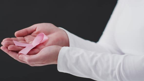 Mid section of woman holding a pink ribbon against black background alt