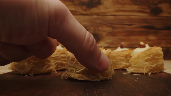 Hand Takes Eastern Sweets on Wooden Background Closeup