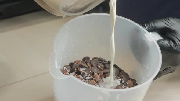 a Pastry Chef Pours Hot Milk Into a Container with Chocolate Tablets for Making Chocolate Glaze