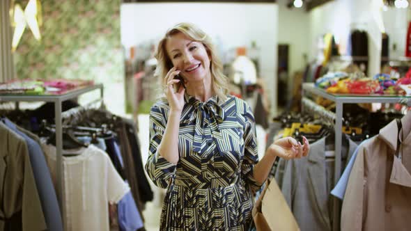 Happy Middle Aged Woman Is Talking on Mobile Phone at Clothing Store at Mall and Smiling