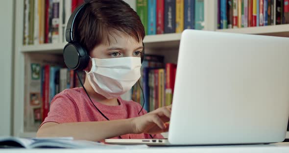 Child Wearing Face Mask and Headphones Working on Notebook