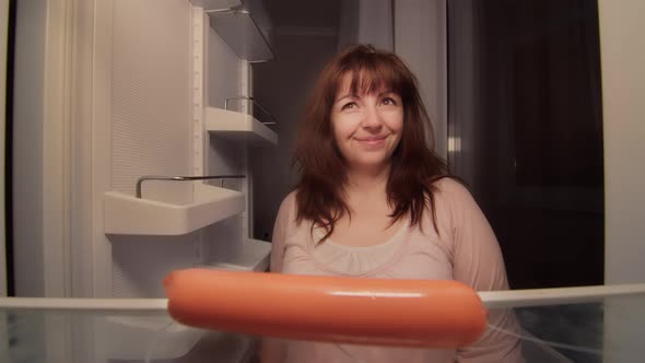 Brunette Woman Takes a Sausage From the Fridge at Night Hungry Woman