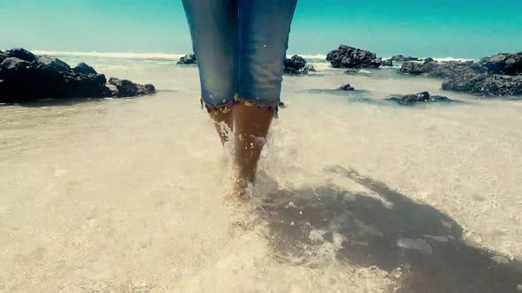 Close up of woman’s feet and legs walking out the sea water splashing the camera - summer holiday alt