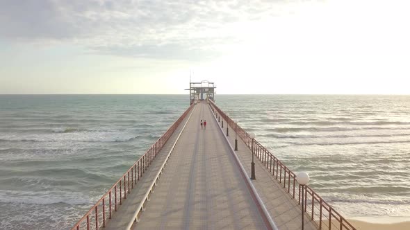 Aerial view of teen couple boy and girl walk by hand on pier in sea at sunset. Summer vacation, love