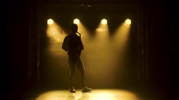 Silhouette a Young Stylish Guy Plays the Golden Shiny Saxophone in the Yellow Spotlights on Stage alt