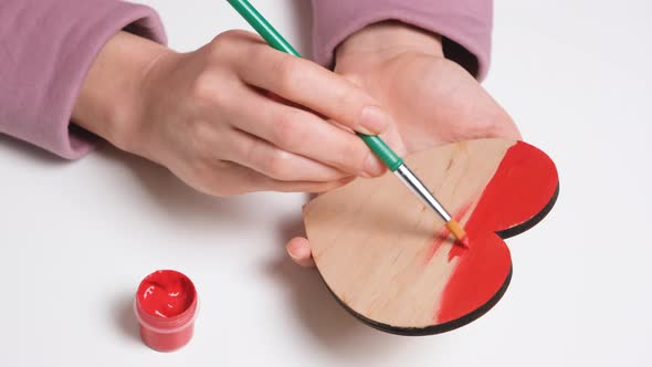 Hand Paints a Wooden Heart in Red