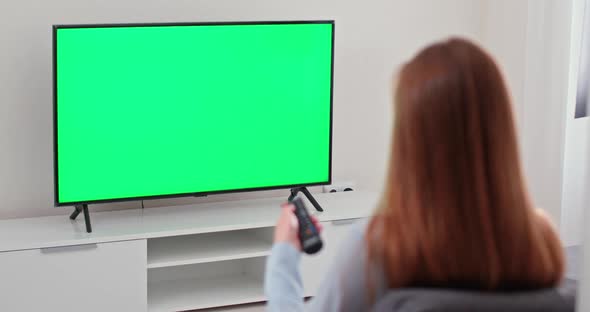 Girl Is Sitting on the Sofa in the Living Room and Watching TV, Green Screen, the Girl Switches alt