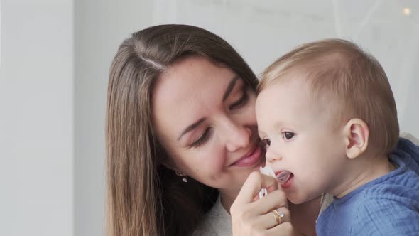 Close-up of a beautiful loving mother in a dress, who is standing at the window with a baby in her a alt