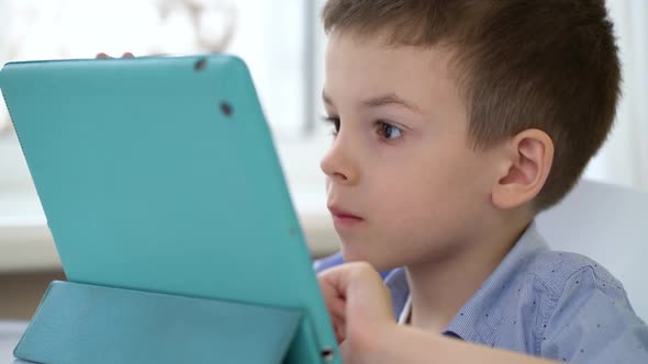 Preschooler Sits at a Table and Looks at a Digital Tablet