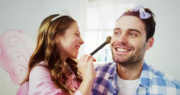 Girl dressed up in a fairy costume applying make-up on fathers face alt