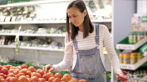 Young Woman in Denim Overall is Selecting Fresh Tomatoes at Grocery Store alt