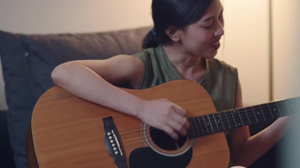 Asian woman trying learning guitar while staying at home.