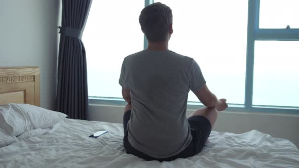 A Man Meditates on Bed While Looking Out the Window