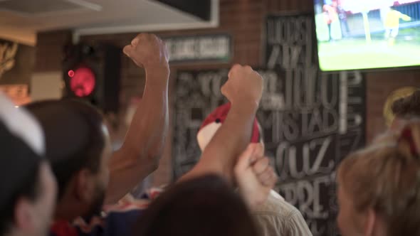Football fans excitedly cheering while watching televised match at sports bar alt