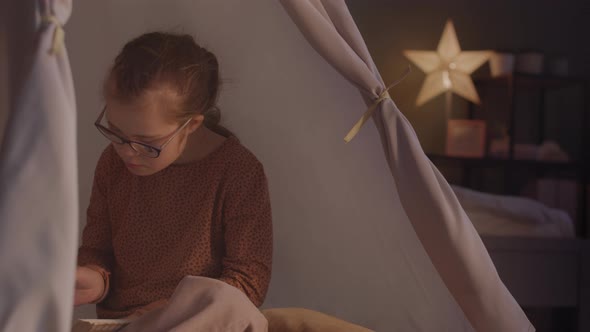 Girl Reading Book in Dark in Tent at Home alt