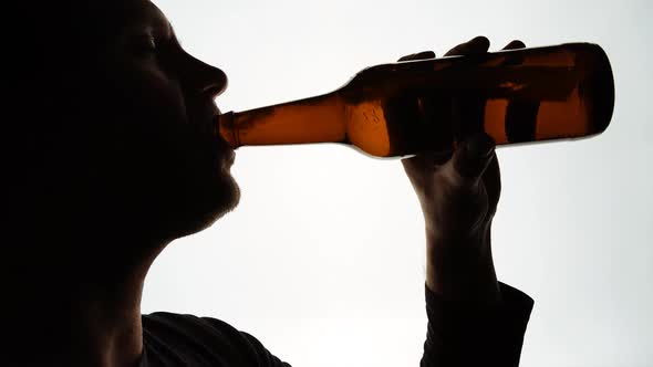The Silhouette of Male head drinking from a brown bottle