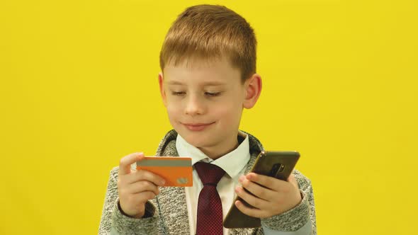A Caucasian boy of 7-8 years old uses a children's bank card and a mobile phone alt