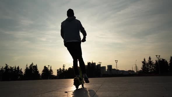 Silhouette of Man on the Electric Scooter on the Sunset in the City alt
