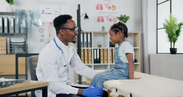 Doctor Talking with Joyful Little Girl in Modern Medical Office and Giving Her High Five alt