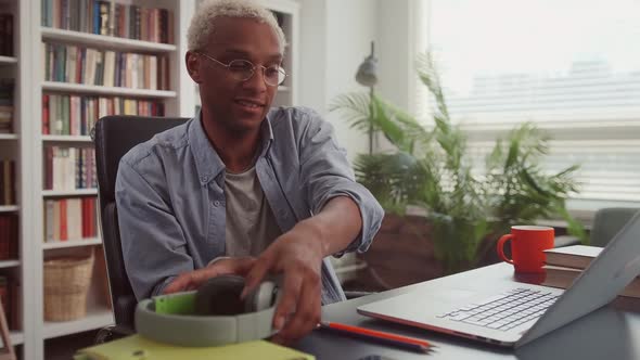 African Man Opening Laptop Wearing Wireless Headphones and Starting His Workday alt
