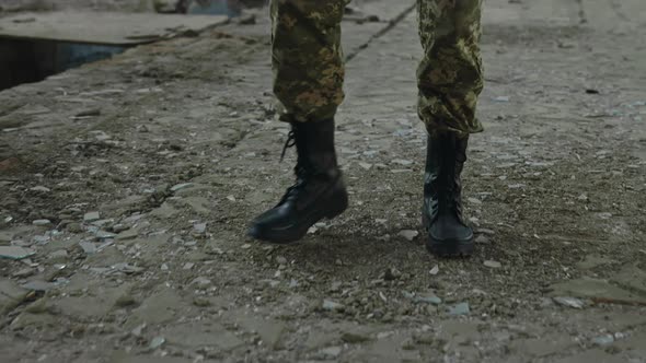 Soldier in Uniform and Boots Walking on Destroyed Factory alt