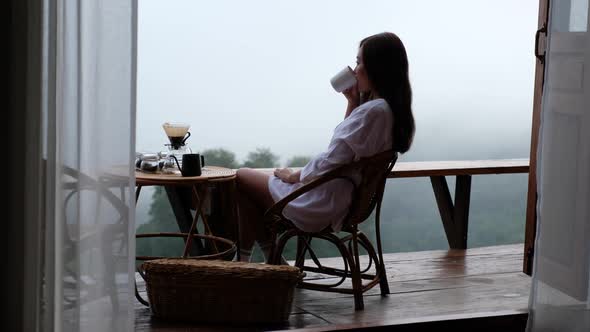 A woman drinking drip coffee and enjoy watching a beautiful nature view on foggy day