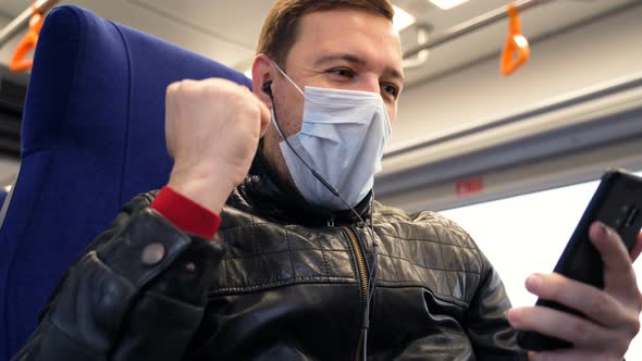 Excited Male Wearing Medical Face Mask Looks at Phone and Celebrates Big Win Financial Good News alt