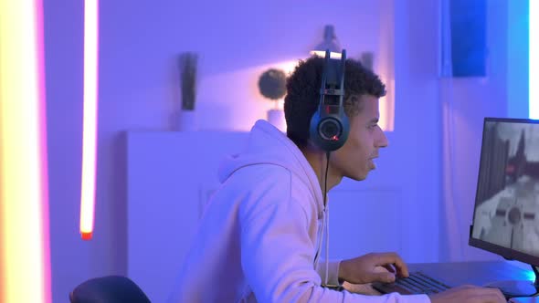 Medium Shot of Young Black Gammer in Headphones Playing in Online Shooter alt