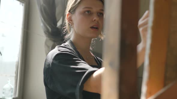 Woman in Dirty Apron Draws Picture on Canvas in Studio alt