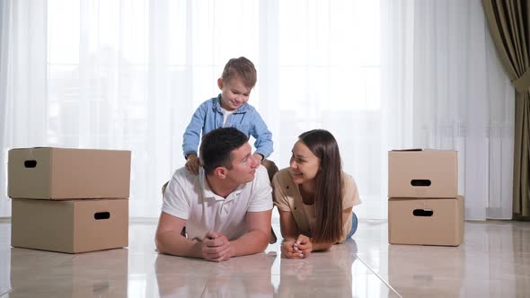 Child Sits on Father Back Lying on Light Floor in New House alt