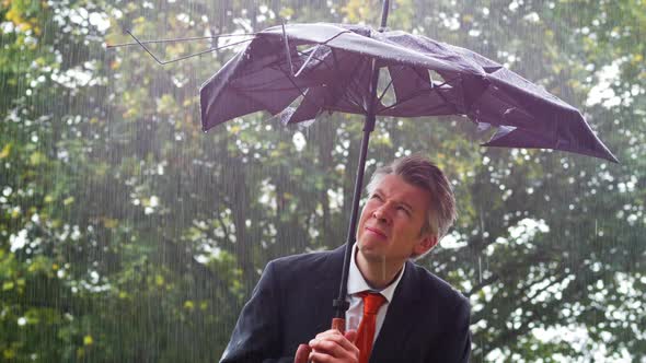 Businessman Sheltering Underneath a Broken Umbrella in the Rain