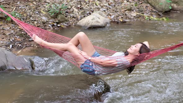 A young asian woman lying and relaxing in hammock in waterfall stream