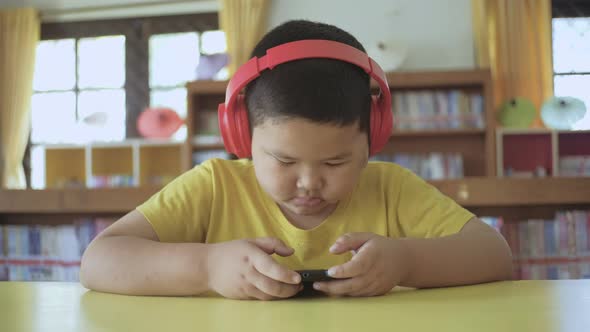 Asian little boy with red headphones using smartphone at home by maxxasatori