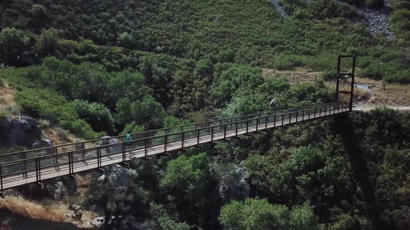 Drone Shot following an active man running on an outdoor hanging suspension bridge above Bear Canyon alt
