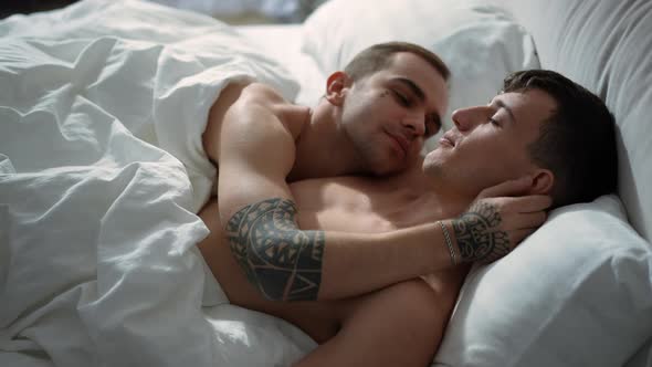 Side View Young Men Sleeping in Bed Together Waking Up in the Morning Kissing Cheek alt
