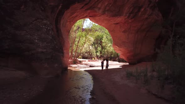 A man getting down on one knee and proposing to his girlfriend under a beautiful huge red rock Arch alt