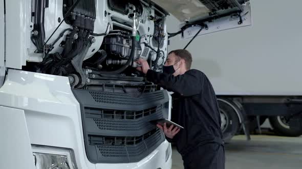 Engineer in protective mask stands in repair shop using modern device tablet alt