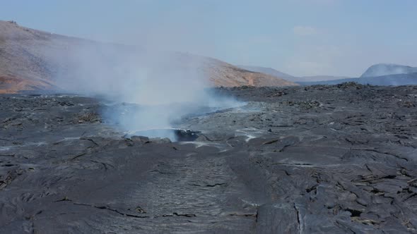Slide and Pan Footage of Smoke Coming Out From Hole in Layer of Cooling Lava in New Lava Field alt