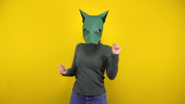 Young Woman in a Cardboard Jackal Mask Dances on a Yellow Background. Woman in a Green Sweater and alt