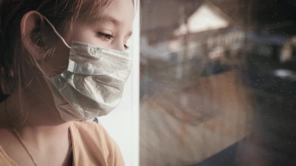 Little Girl in a Protective Mask Sits in Quarantine at Home alt