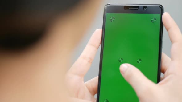 Asian woman using smartphone with green screen while standing at a public park.