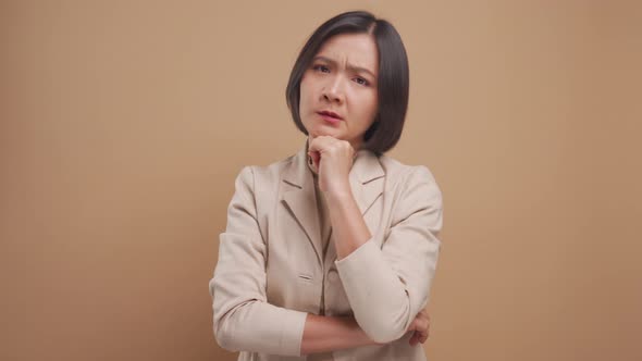 Asian business woman feel confused standing and looking at camera isolated over beige background