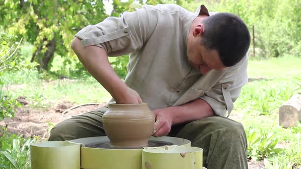 Male Potter Caucasian Ethnicity in a Work Shirt Creates a Large Clay Pot on a Round Rotating Machine alt